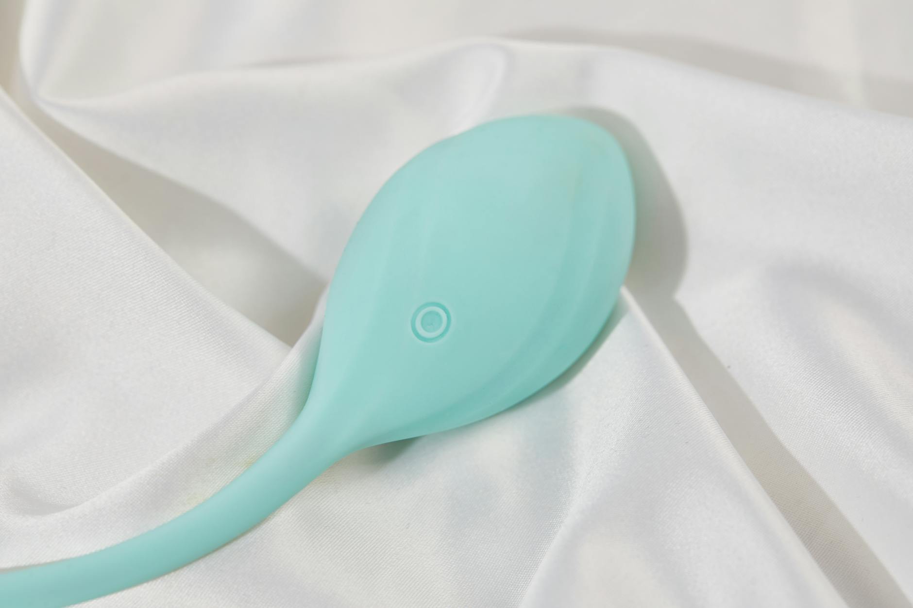 A sleek teal lemon vibrator resting on white silk fabric