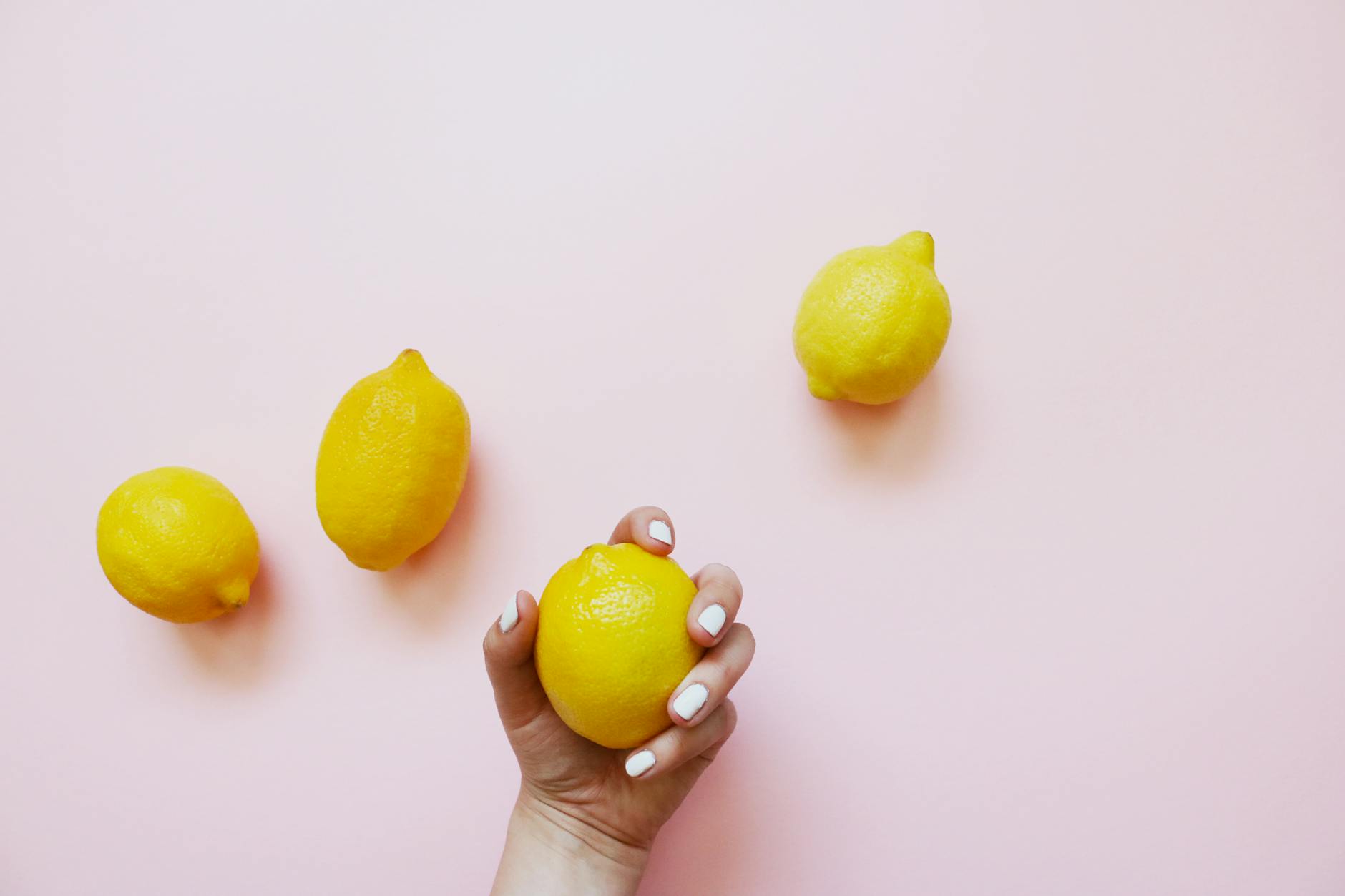 A hand holding a lemon against a soft pink background, representing the gentle suction technology of the Lem vibrator.