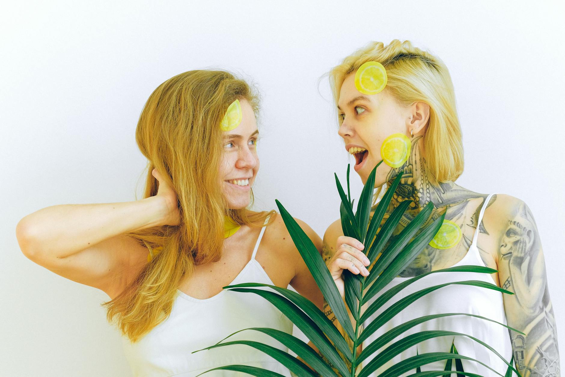 Two women smiling with lemons and tropical plants, expressing joy and comfort indoors