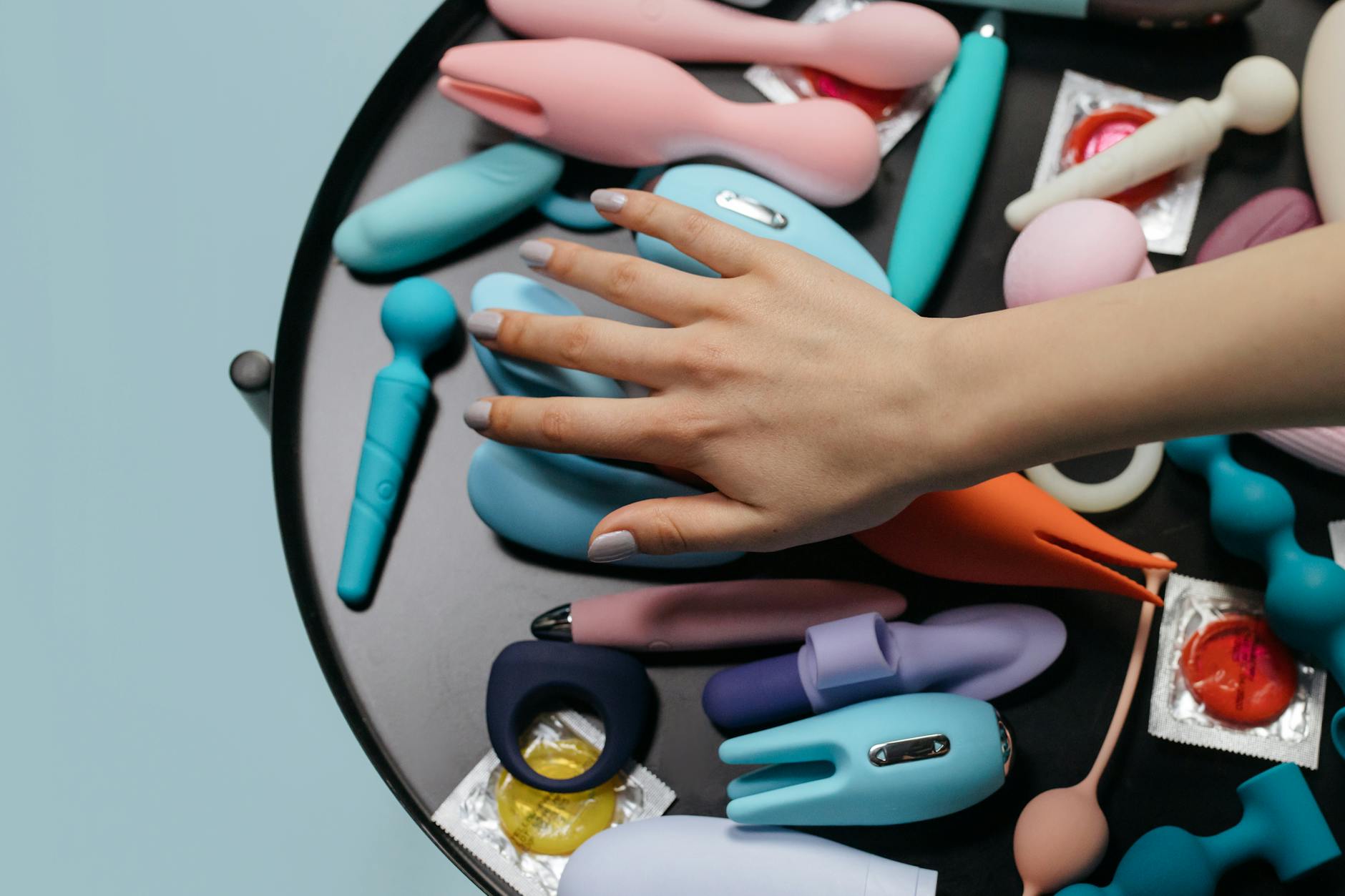 A hand reaching over a variety of colorful clitoral vibrators and lemon suction toys arranged on a table.