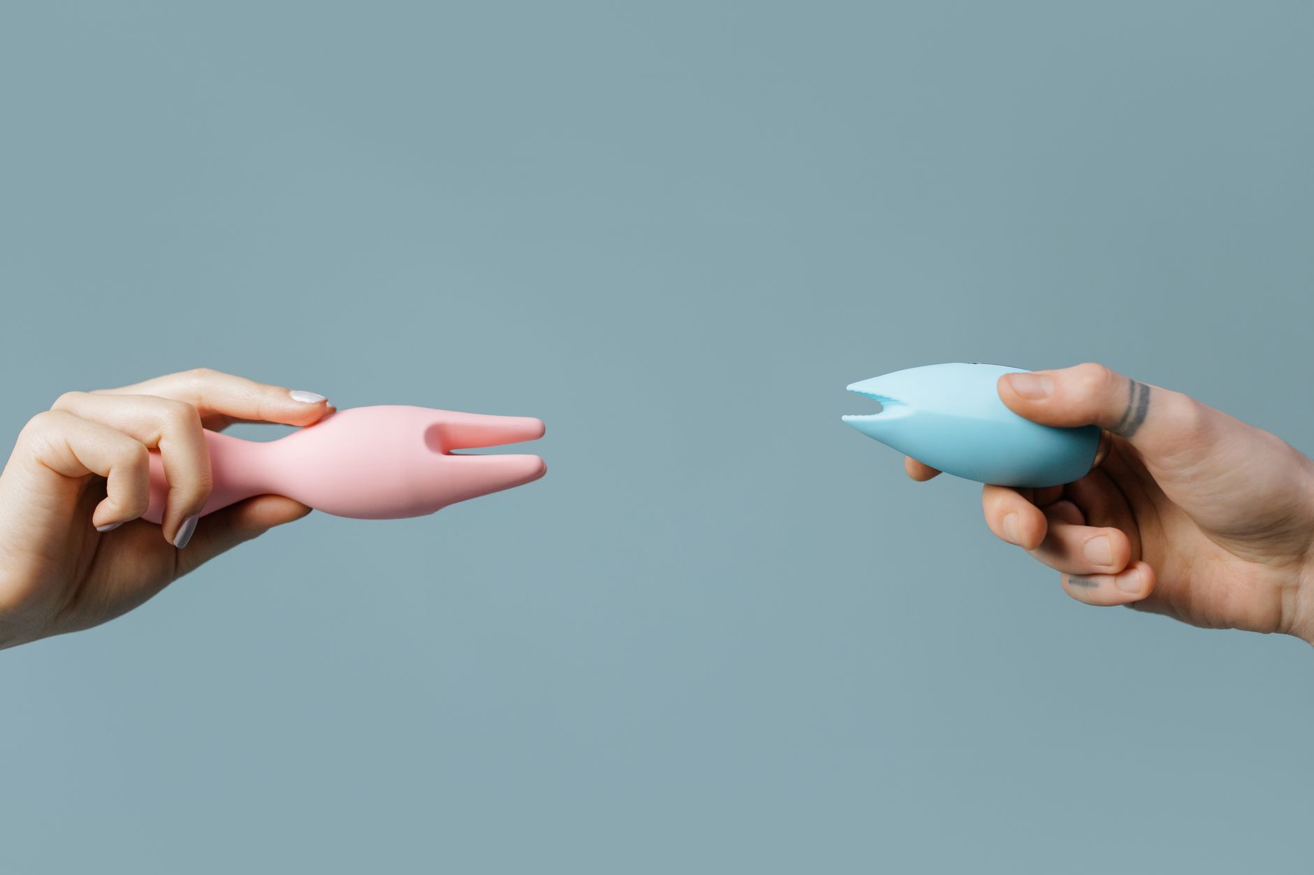 Hands holding pink and blue silicone vibrators against a pastel background, representing safe pleasure for all bodies.