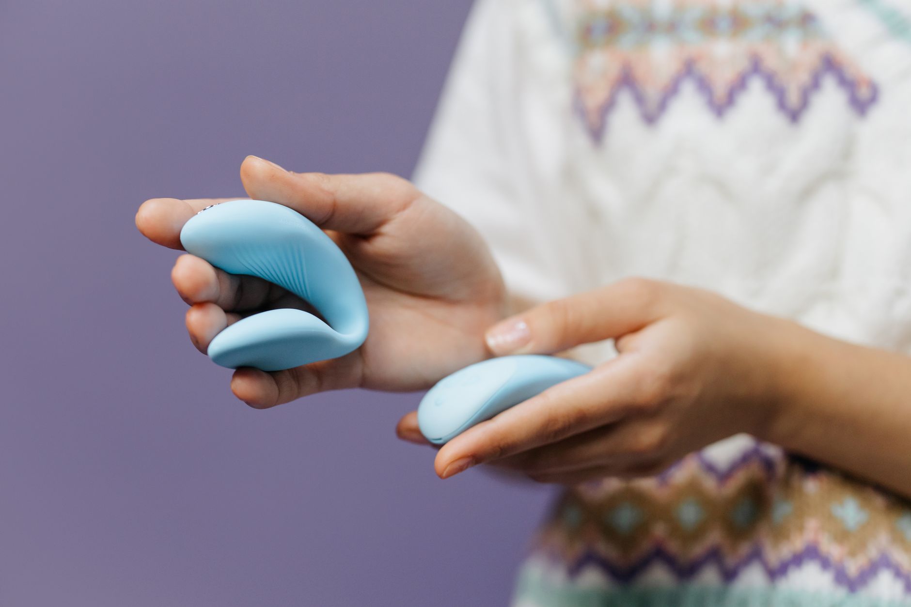 Close-up of hands holding a sleek blue lemon vibrator against a purple background.