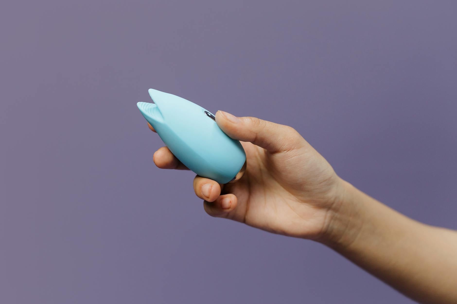 Blue silicone lemon vibrator held gently in hand against purple background