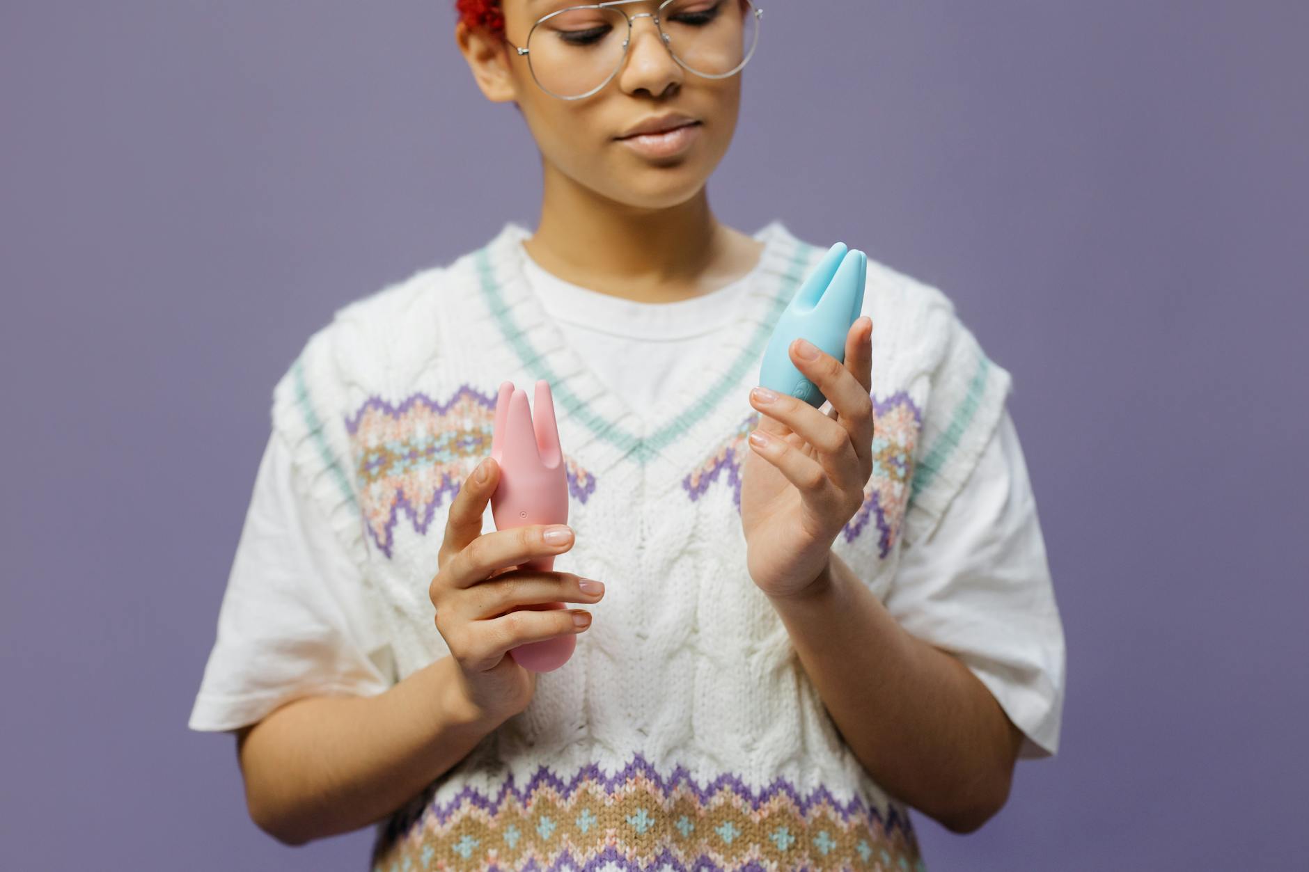 Woman with eyeglasses thoughtfully holding colorful silicone vibrators, exploring sensation and pleasure.