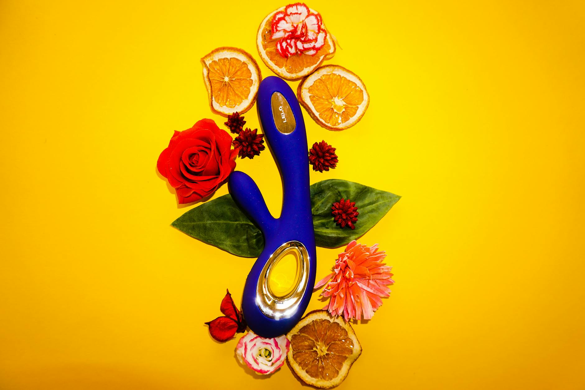 A lemon vibrator surrounded by flowers and citrus on a bright background, symbolizing the gentle reconnection to pleasure.