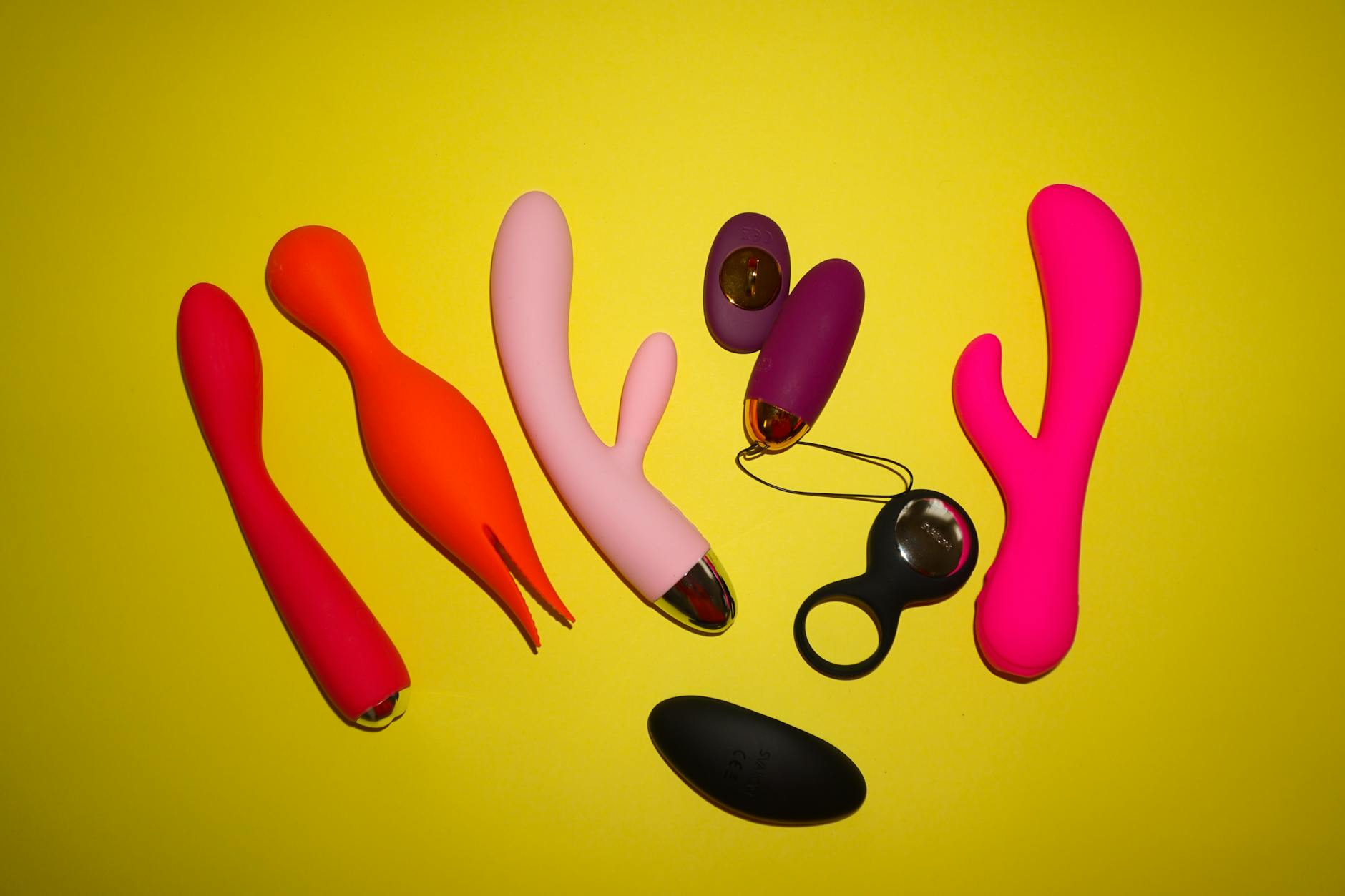 Colorful vibrators and adult toys displayed on a bright yellow background in studio lighting